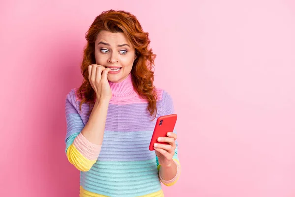 Foto portret van vrouw in paniek bijten nagels houden telefoon in een hand geïsoleerd op pastel roze gekleurde achtergrond — Stockfoto