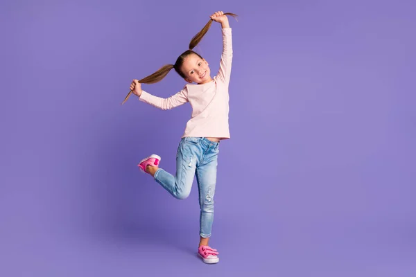 Полноразмерная фотография безкровной счастливой девушки, держащей за руки косички в джинсовом свитере, изолированном на фиолетовом цветовом фоне — стоковое фото