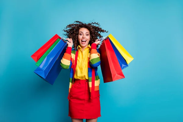 Fénykép a gyönyörű trendi elegáns barna hullámos hajú lány viselni piros szoknya izgatott vásárlás emelés táskák elszigetelt kék színű háttér — Stock Fotó