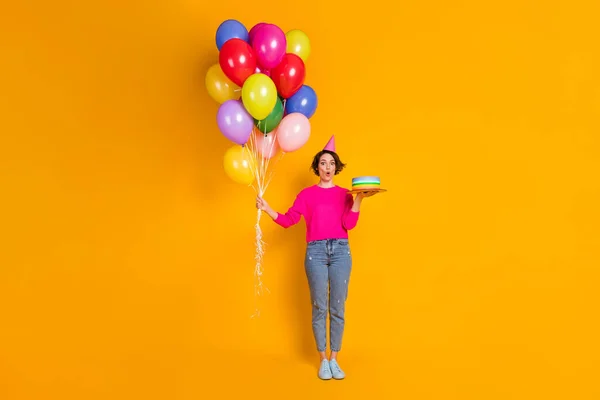 Foto de comprimento total de menina surpreendida segurar bolo de aniversário muitos balões usam camisola de cone isolado fundo de cor brilhante — Fotografia de Stock