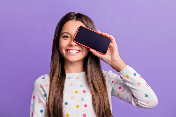 Bir gözünü telefonla kaplayan mutlu bir kızın fotoğrafı. Parlak mor arka planda izole edilmiş boş bir alan. — Stok fotoğraf