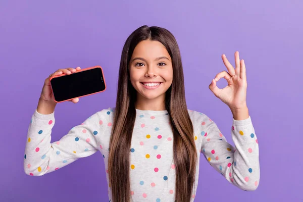 Foto retrato de niña sosteniendo el teléfono con copyspace haciendo ok-signo aislado sobre fondo de color púrpura brillante —  Fotos de Stock