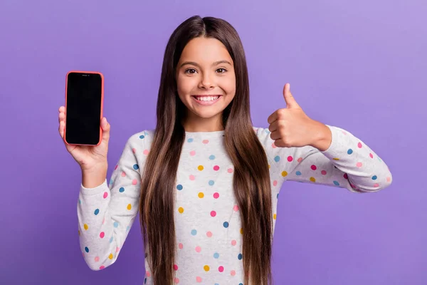 Foto retrato de menina morena dando polegar para cima segurando telefone com espaço em branco em uma mão isolada no fundo colorido roxo brilhante — Fotografia de Stock