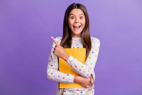 Retrato fotográfico de una alumna sorprendida que mantiene el cuaderno amarillo apuntando al espacio en blanco aislado sobre un vibrante fondo de color violeta — Foto de Stock
