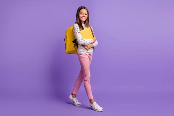 Foto de cuerpo entero tamaño de la pupila femenina caminando abrazando libro llevando bolsa amarilla sonriendo aislado sobre fondo violeta vívido —  Fotos de Stock