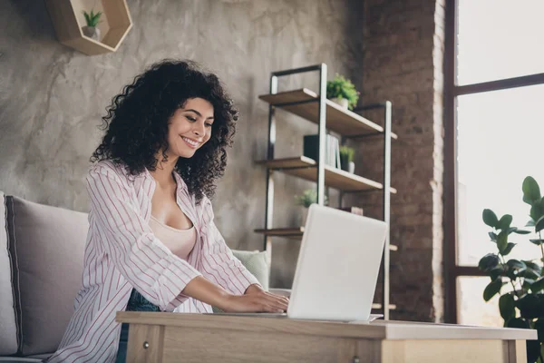 Retrato fotográfico de una chica positiva trabajando en un portátil sentado en un cómodo sofá gris en el interior — Foto de Stock