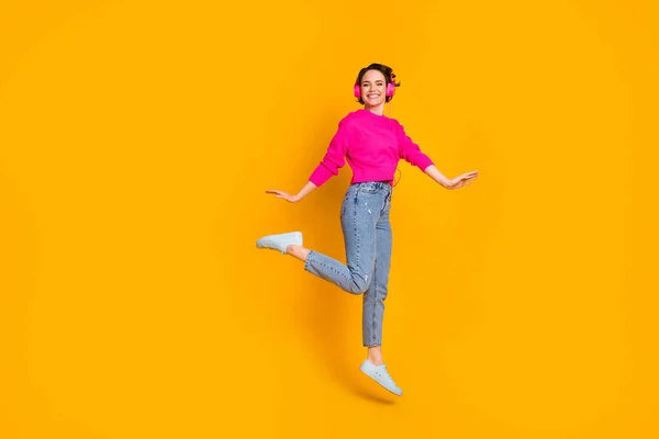 Full length photo of pretty funky lady jump high listen earphones wear pink πουλόβερ τζιν παπούτσια απομονωμένο κίτρινο χρώμα φόντο — Φωτογραφία Αρχείου