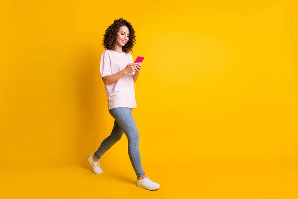 Foto de cuerpo de cuerpo entero de mujer millennial usando aplicación móvil caminando aislado sobre fondo de color amarillo vibrante con copyspace — Foto de Stock