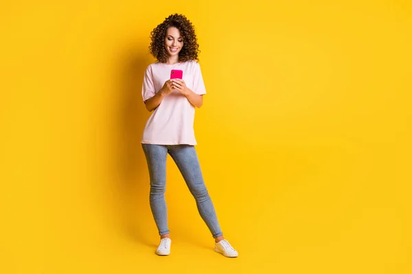 Foto de cuerpo de cuerpo entero de mujer hipster escribiendo sms en el teléfono inteligente sonriendo aislado en fondo de color amarillo vivo con copyspace — Foto de Stock