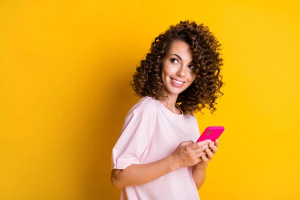 Foto portret van krullend nieuwsgierig meisje houden smartphone kijken naar lege ruimte geïsoleerd op levendige gele kleur achtergrond — Stockfoto