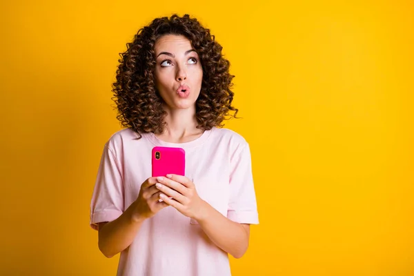 Foto retrato de chica de ensueño sosteniendo el teléfono en dos manos mirando el espacio en blanco aislado sobre fondo de color amarillo vivo — Foto de Stock