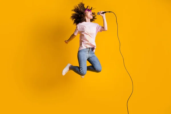 Photo portrait full body view of ecstatic woman jumping up singing into microphone isolated on vivid yellow colored background — Stock Photo, Image