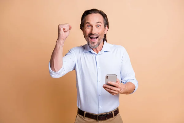 Foto de homem barbudo segurar celular levantar punho aberto boca desgaste camisa isolado cor bege fundo — Fotografia de Stock