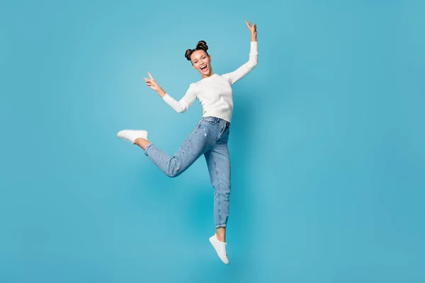 Foto de longitud completa de niña salto risa espectáculo dos v-signos de desgaste blanco jersey jeans zapatillas aisladas de color azul fondo — Foto de Stock