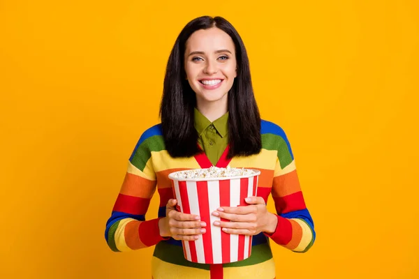 Photo de heureux positif jeune fille sourire tenir boîte pop-corn regarder le film isolé sur fond de couleur jaune — Photo