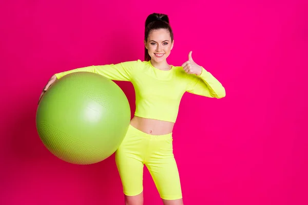 Foto de la deportista positiva mantenga fitball mostrar el símbolo thumb-up aislado sobre el fondo de color rosa brillante —  Fotos de Stock