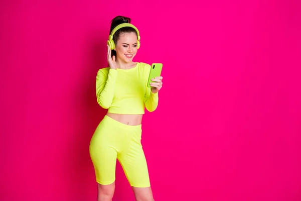 Positieve jonge sportvrouw gebruik smartphone luister playlist headset slijtage gele shorts geïsoleerd op roze heldere kleur achtergrond — Stockfoto