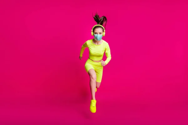 Фотографія повної довжини тіла жінки бігуна, що стрибає високо в носінні маски для обличчя ізольовані на яскравому кольоровому фоні фуксії — стокове фото