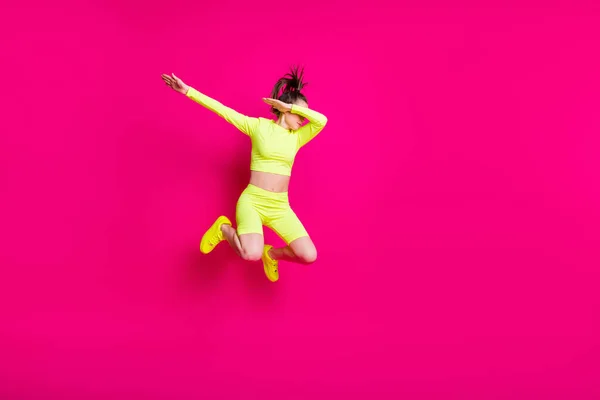 Volledige lichaamslengte foto van springen jong meisje dragen gele sportkleding tonen hype geïsoleerd op fel roze kleur achtergrond — Stockfoto