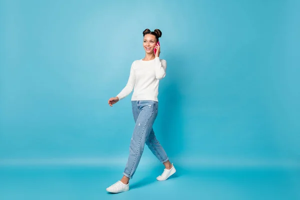 Foto av positiv flicka gå hålla telefonen har konversation bära vit tröja jeans skor isolerad blå färg bakgrund — Stockfoto