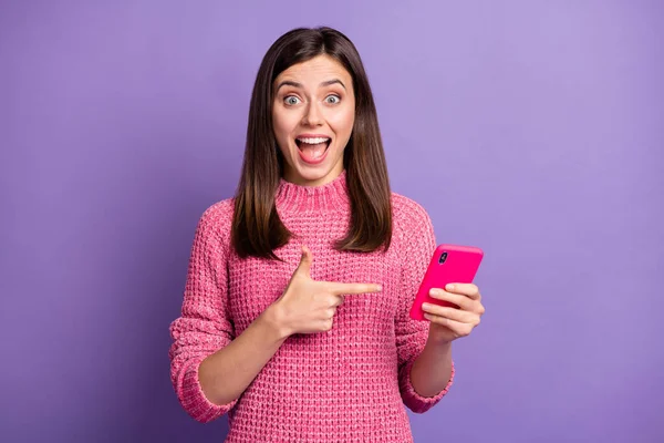 Фотографічний портрет здивованої жінки-брюнетки, що вказує на палець мобільного телефону, який дивиться відкритий рот ізольований на яскраво-фіолетовому кольоровому фоні — стокове фото