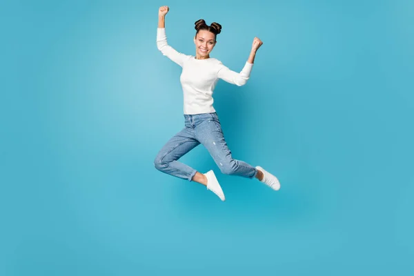 Фотографія дівчини, що стрибає підняти кулаки, носить білий светр джинси кросівки ізольовані синій колір фону — стокове фото
