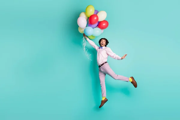 Acayip zıplayan adam renkli helyum balonları tutuyor. Hava yükseliyor. Turkuaz arka planda izole edilmiş resmi kıyafetler giyiyor. — Stok fotoğraf