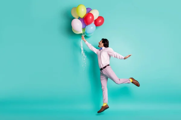 Portret van springende jongeman houden kleurrijke helium ballonnen dragen formele outfit gele sokken geïsoleerd op turquoise achtergrond — Stockfoto