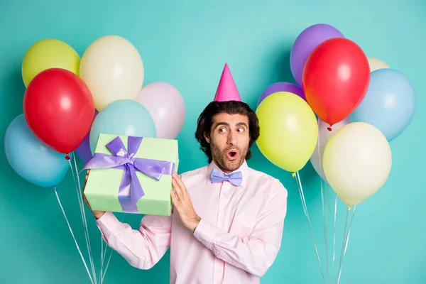 Foto de caballero curioso mantenga la caja de regalo globos de helio coloridos usan tapa de cono aislado en el fondo de color turquesa — Foto de Stock