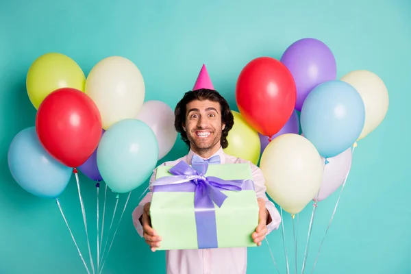 Foto de homem positivo amigável dando giftbox balões de hélio coloridos vestido formalwear cone isolado no fundo de cor turquesa — Fotografia de Stock