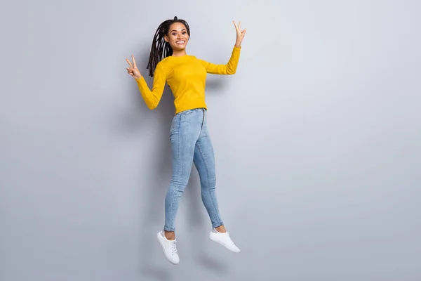 Foto de longitud completa de la joven alegre feliz sonrisa positiva salto espectáculo v-signo de desgaste jeans aislados sobre fondo de color gris — Foto de Stock