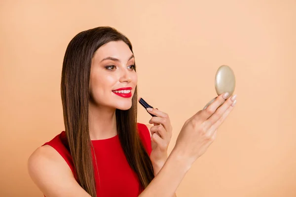 美しい女性ホールドルックミラーのプロフィール側の写真は、パステルベージュの色の背景に隔離された唇赤いザーメンを適用します — ストック写真