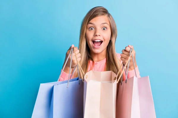 Retrato fotográfico de una niña sosteniendo bolsas con la boca abierta aislada sobre fondo de color azul pastel —  Fotos de Stock