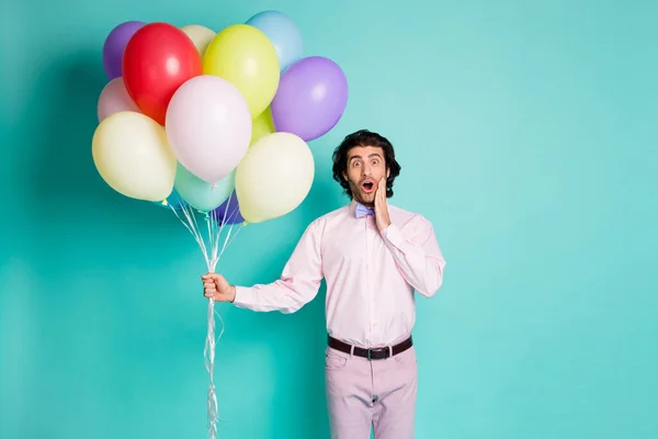 Ritratto di sorpreso sorridente uomo bocca aperta toccare zigomo vestito formale camicia pantaloni tenere palloncini colorati isolati su sfondo di colore turchese — Foto Stock