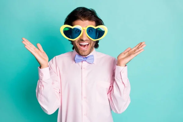 Foto de hombre joven sorprendido usar traje formal en forma de corazón sol especificaciones levantar brazos aislados sobre fondo de color turquesa —  Fotos de Stock