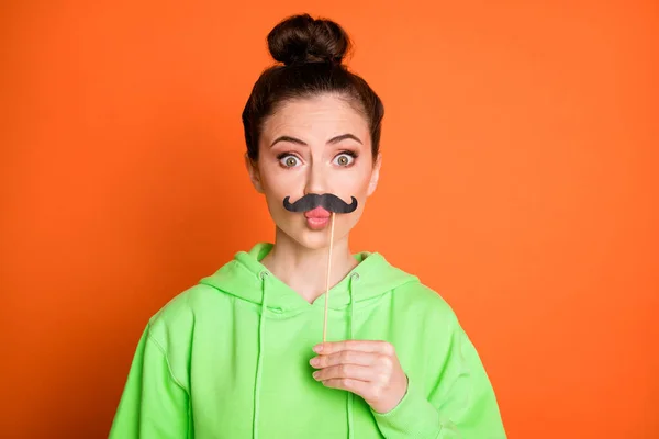 Foto de divertida mujer joven sorprendida usar verde sudadera con capucha labios pucheros sosteniendo bigote aislado color naranja vivo fondo —  Fotos de Stock