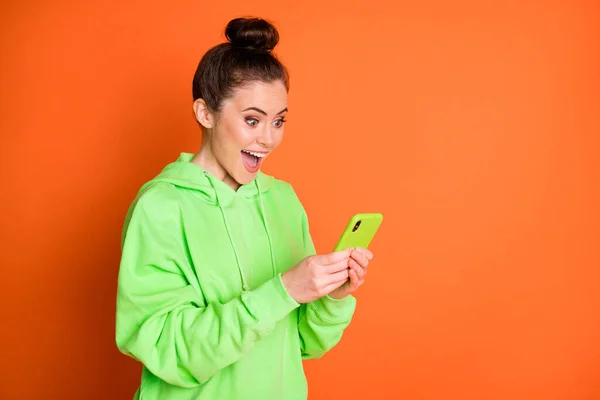 Foto ritratto di una ragazza scioccata che tiene il telefono in due mani isolate su un vivido sfondo di colore arancione con spazio vuoto — Foto Stock