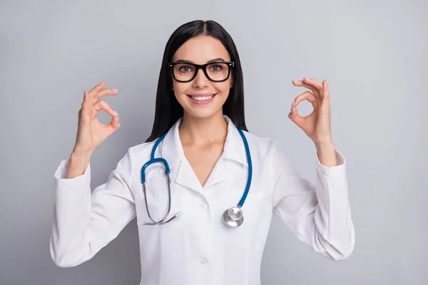 Foto von Arzt Mädchen strahlendes Lächeln heben zwei okey Zeichen tragen Brille Stethoskop weiße Uniform isoliert graue Farbe Hintergrund — Stockfoto