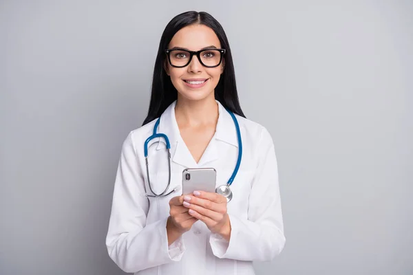 Foto des Arztes Mädchen halten Smartphone-Look Kamera tragen Stethoskop-Brille weiße Uniform isoliert graue Farbe Hintergrund — Stockfoto