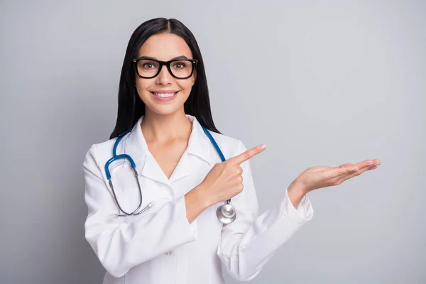 Photo of doctor girl direct finger palm hold empty space wear stetoskop eyewear white uniform isolated grey color background — Zdjęcie stockowe