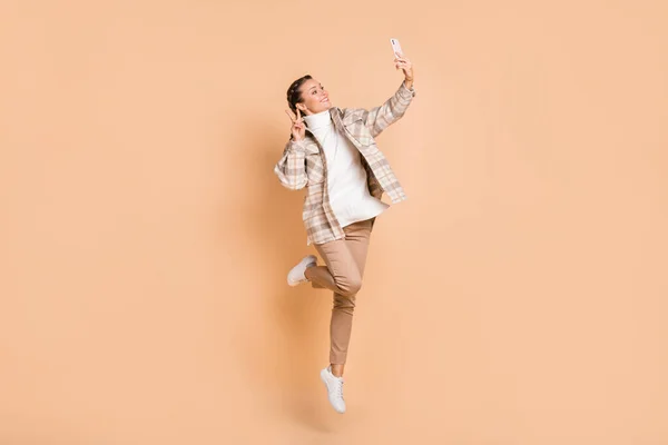 Full storlek profil foto av optimistisk flicka hoppa gör selfie show v-tecken bära vit skjorta byxor sneakers isolerade på beige bakgrund — Stockfoto