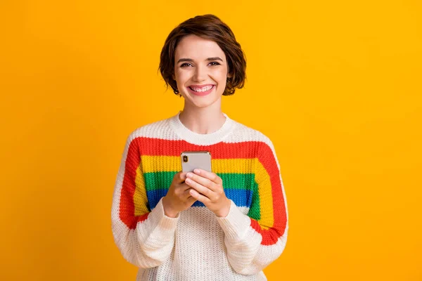 Foto van positief jong meisje houden telefoon stralen glimlach camera slijtage gestreepte trui geïsoleerde gele kleur achtergrond — Stockfoto