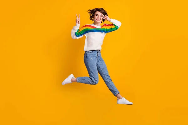 Perfil de tamaño completo de la foto agradable mujer joven salto mostrar v-signo de desgaste suéter jeans calzado aislado sobre fondo amarillo brillante — Foto de Stock