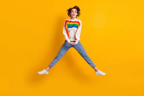 Full size foto di adorabile divertente giovane donna salto indossare maglione arcobaleno jeans denim calzature bianche isolate su sfondo giallo brillante — Foto Stock