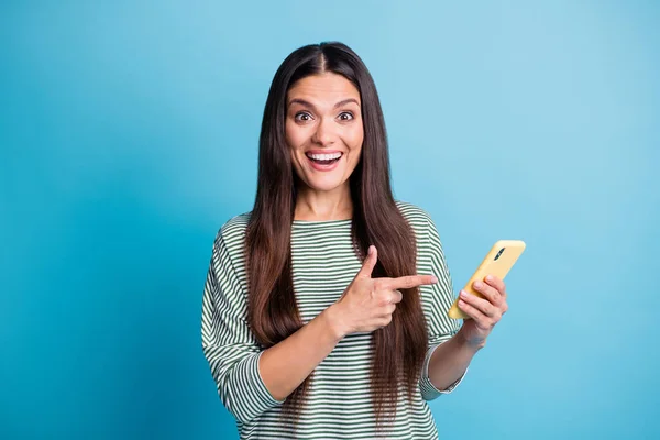 Foto di stupito positivo signora diretta dito telefono usura bianco strisce verdi stile isolato su sfondo di colore blu — Foto Stock