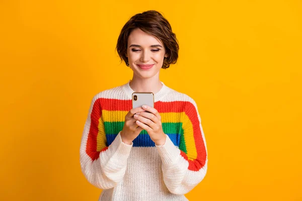 Фото милої молодої дівчини тримає мобільний телефон виглядає екран носити смугастий пуловер ізольований жовтий колір фону — стокове фото