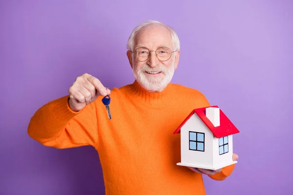 Foto di uomo anziano soddisfatto tenere in mano la piccola casa chiave hanno buon umore isolato su sfondo di colore viola — Foto Stock