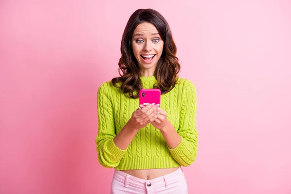 Фото весела збуджена дівчина тримає телефон відкритим ротом у зеленому пуловері ізольований рожевий кольоровий фон — стокове фото
