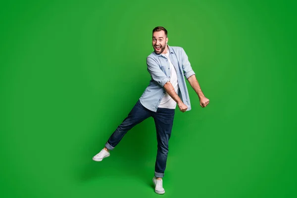 Foto de tamaño completo de chico divertido optimista bailando desgaste azul camisa jeans calzado aislado sobre fondo de color verde —  Fotos de Stock