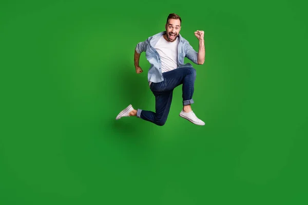 Profilo full size foto di ottimistico funky ragazzo salto indossare camicia blu jeans calzature isolate su sfondo di colore verde — Foto Stock